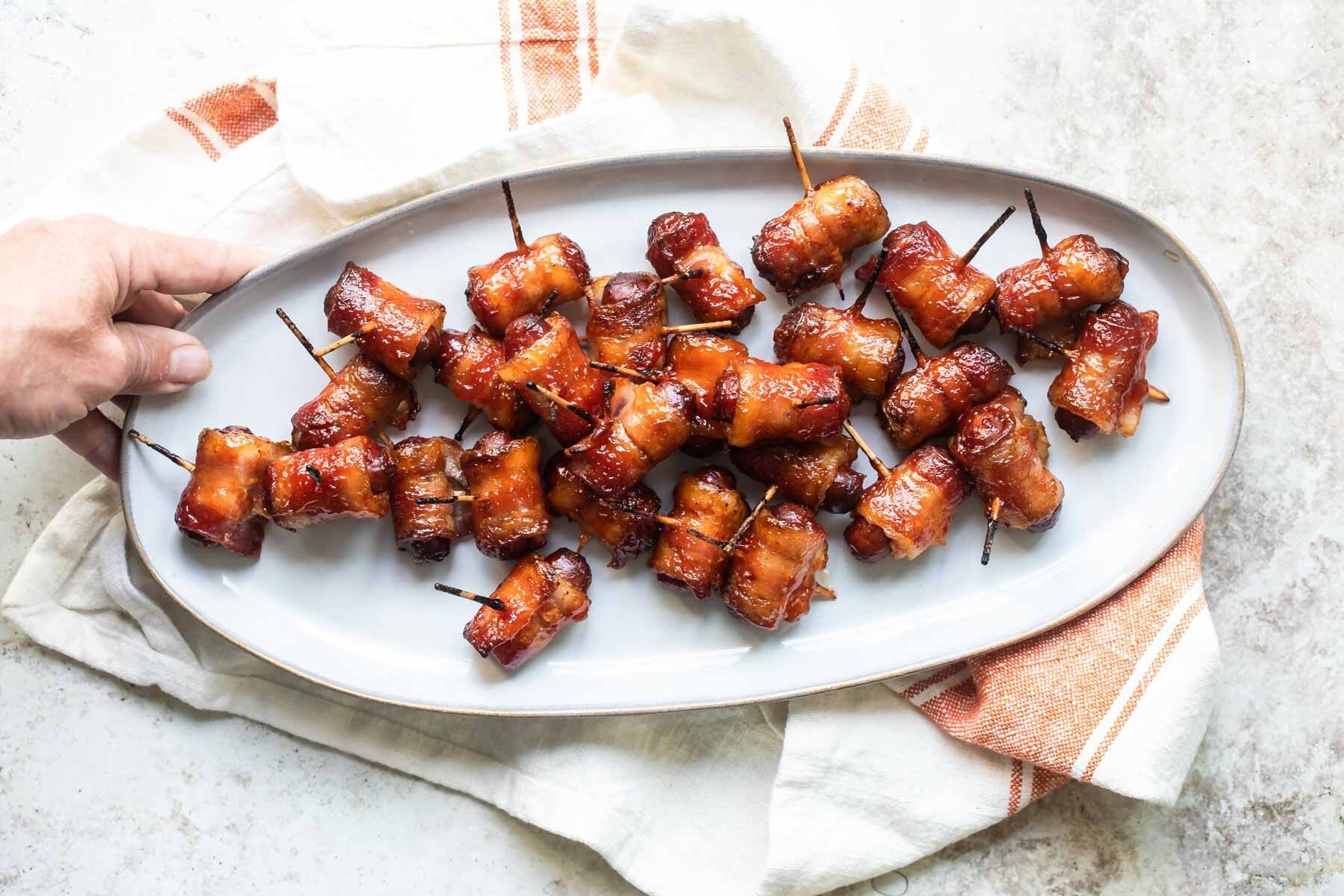 Bacon wrapped smokies on a white serving plate.