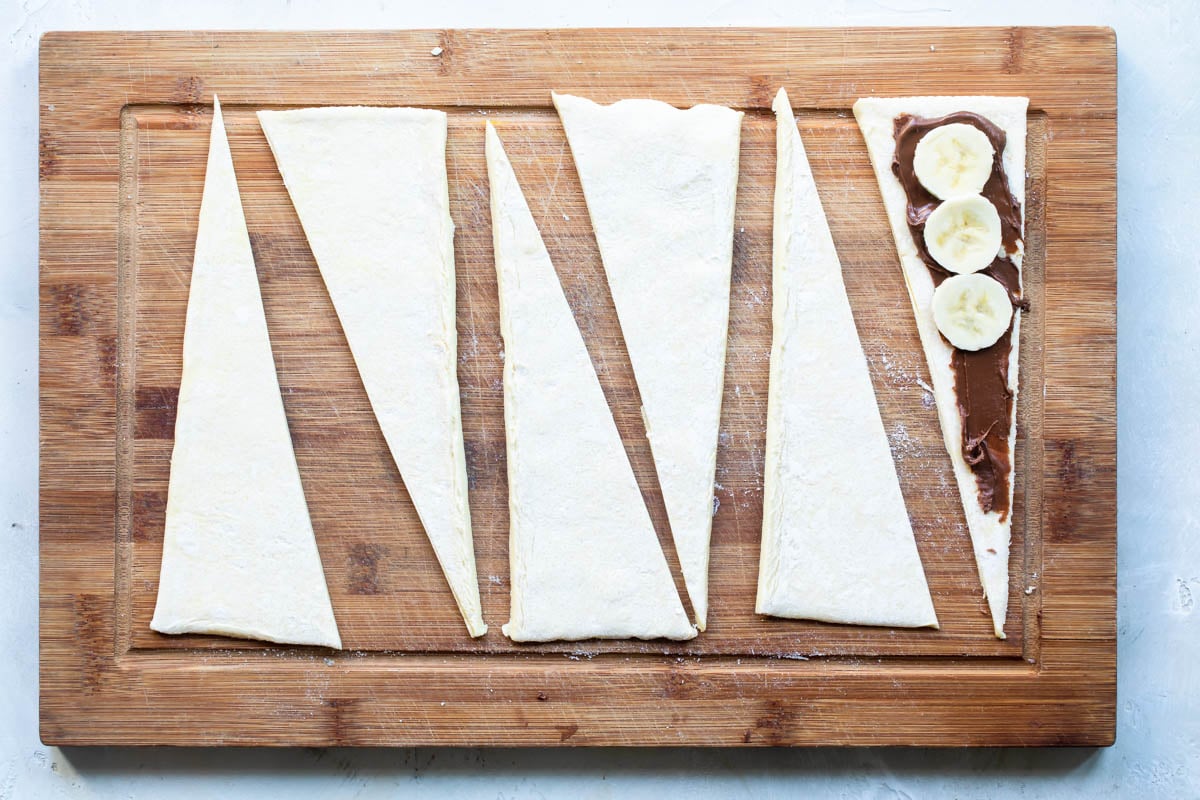 Banana nutella croissants being made on a wooden cutting board.