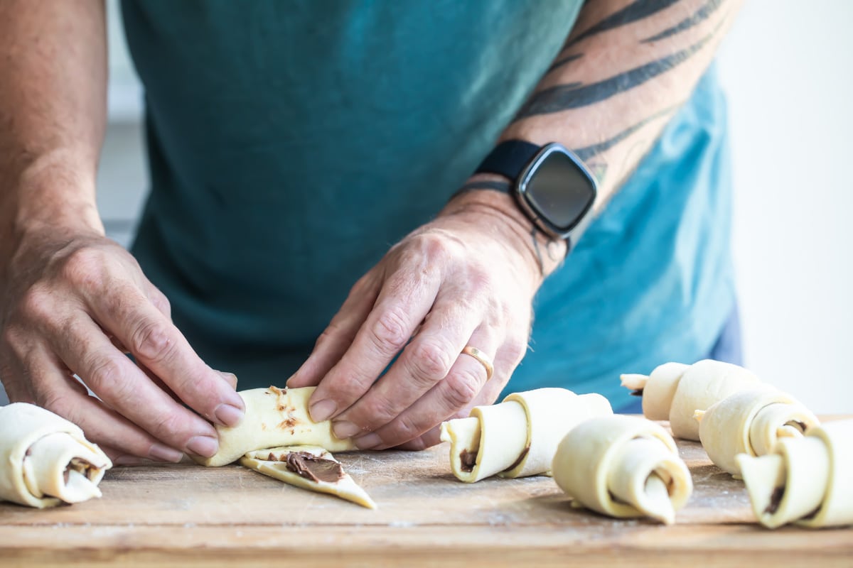 Banana nutella croissants being rolled on a wooden cutting board.