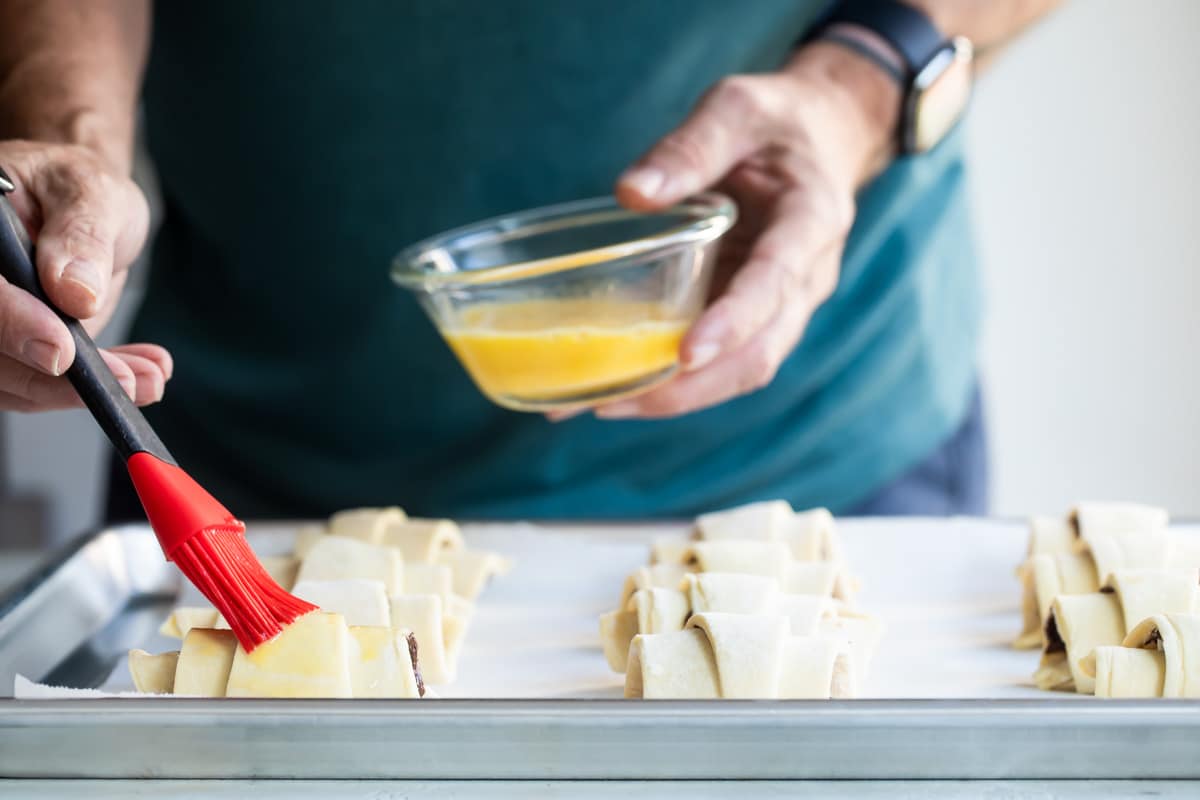 Someone brushing butter on uncooked banana nutella croissants.