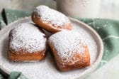 Beignets on a plate next to a coffee mug with liquid in it.