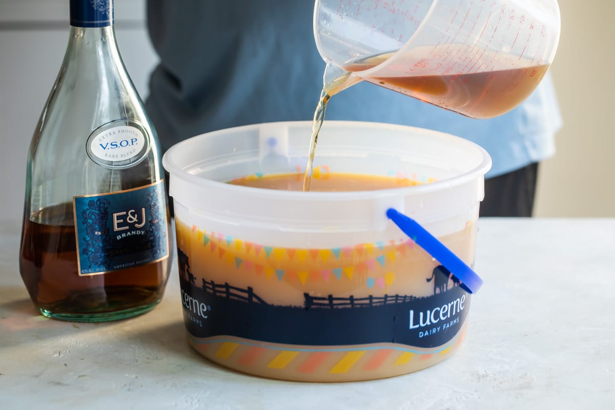 A brown liquid being poured into an ice cream pail.