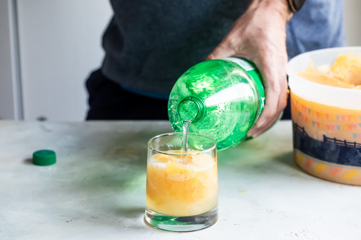 Someone pouring sprite into a cup of brandy slush.