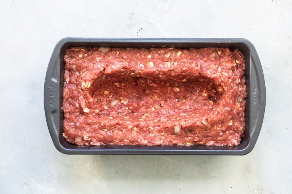 Meatloaf mixture in baking pan with a well for cheese dug out.