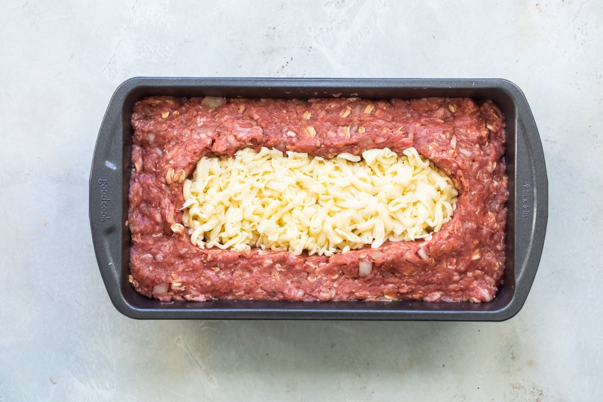 Meatloaf mixture in baking pan with a well of cheese in the middle.