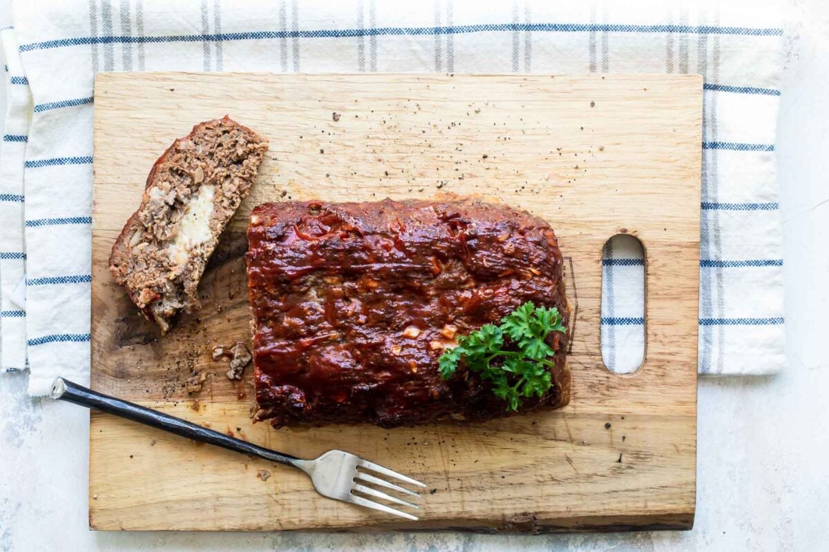 Cheesy meatloaf on a wooden cutting board.