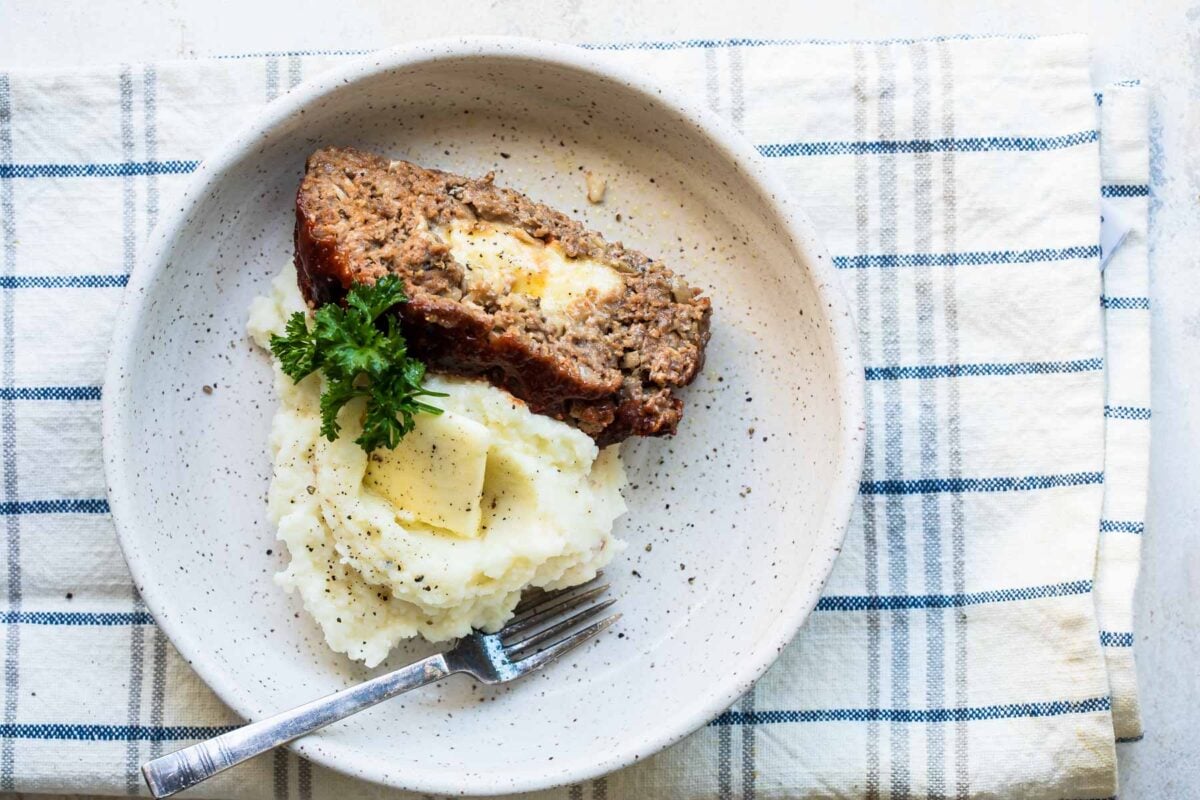 A slice of cheesy meatloaf with mashed potatoes in a low gray bowl.