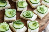 Cucumber sandwiches on a round wooden platter.