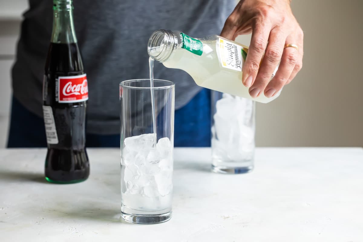 Lemonade being poured over a glass of ice.