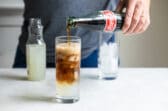 Coke being poured into a half filled glass of lemonade and ice.