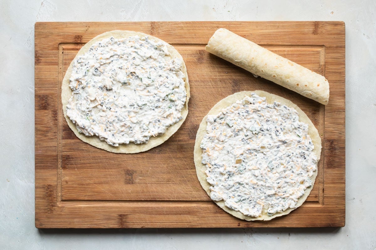 Two tortillas with Mexican filling on them on a wooden cutting board.