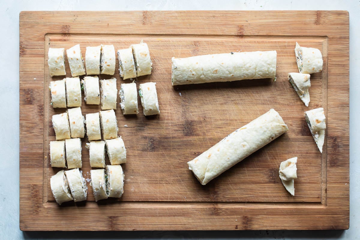 Mexican tortilla roll ups on a board being sliced.