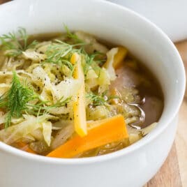 Cabbage Soup in two white bowls on a wooden cutting board.