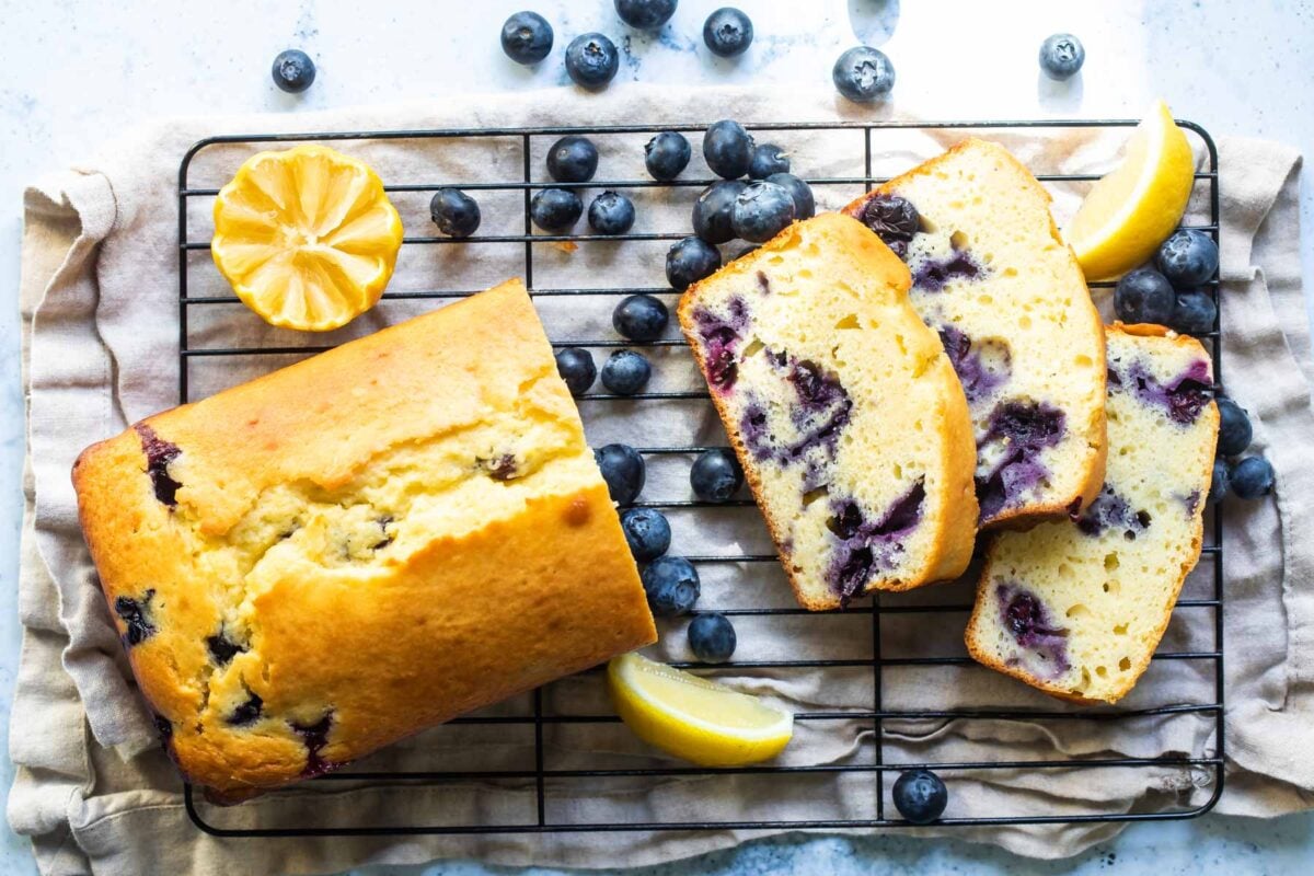 I loaf of blueberry lemon yogurt cake on a cooling rack with three slices cut.