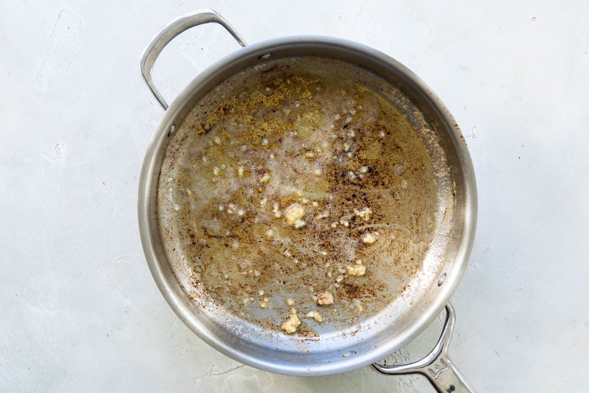 A silver skillet with garlic and other cooked bits in it.