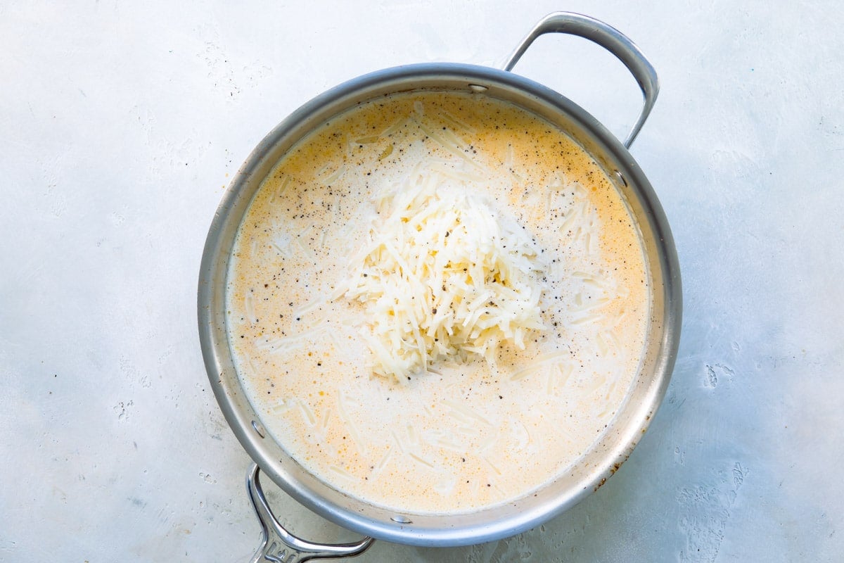 Alfredo sauce being cooked in a silver skillet.
