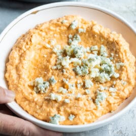 Someone setting down a bowl of cauliflower buffalo dip.