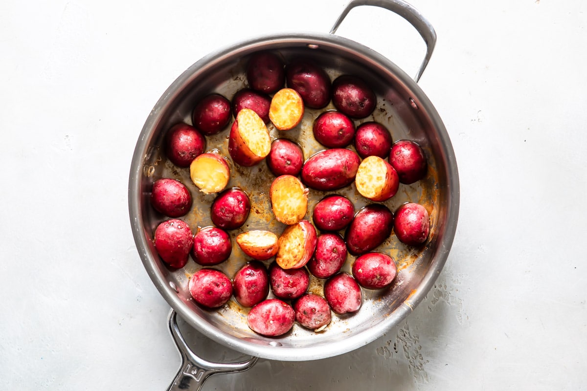 Potatoes cooking in liquid in a silver skillet for chicken vesuvio.