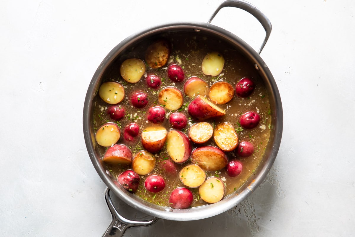 Potatoes cooking in liquid in a silver skillet for chicken vesuvio.