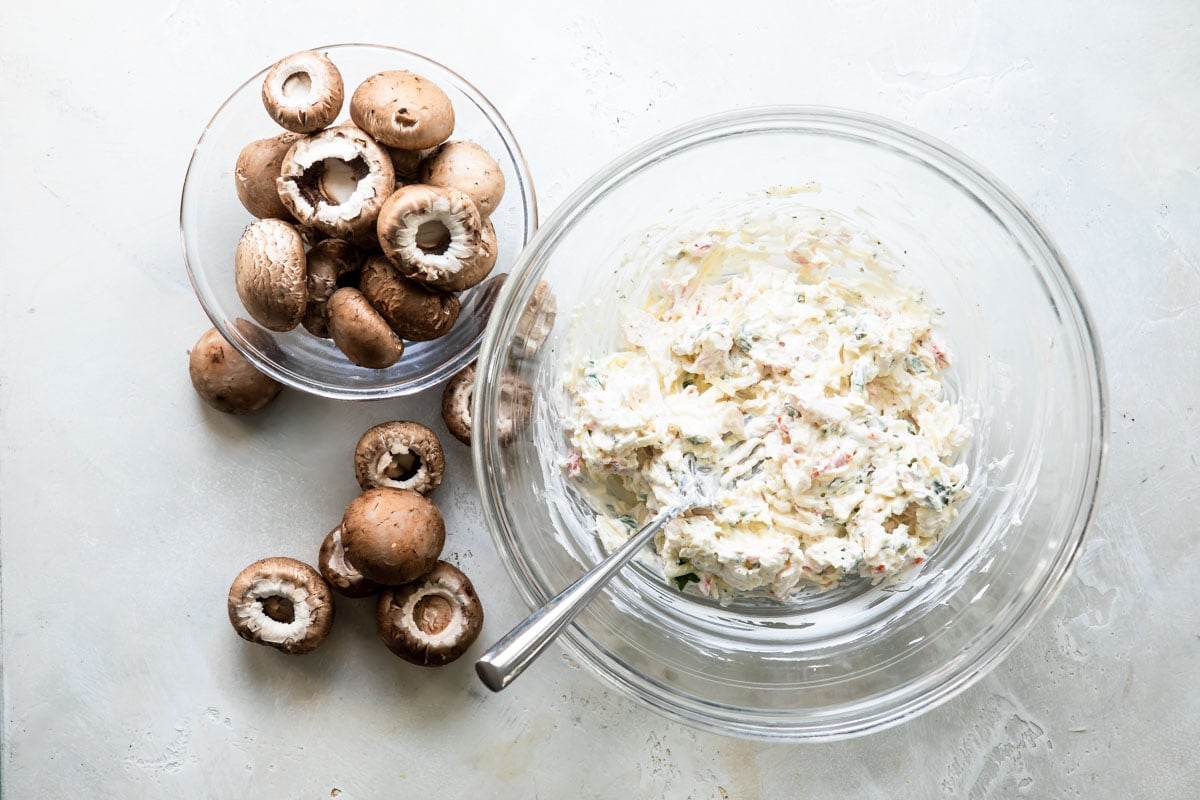 Mushrooms next to a bowl of filling for crab stuffed mushrooms.