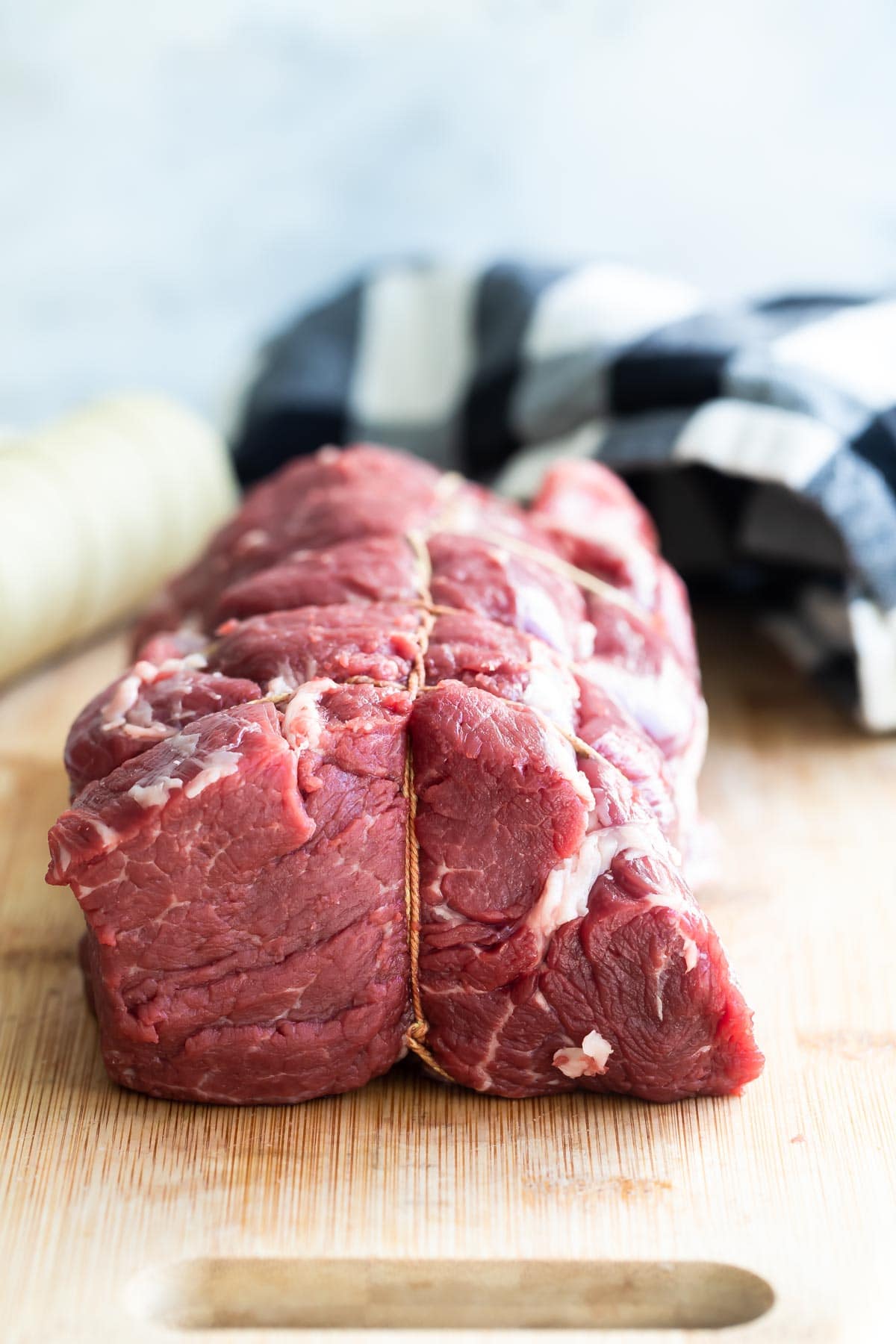 A beef tenderloin tied on a wooden cutting board.