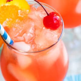 A hurricane cocktail with an orange slice garnish and a blue and white striped straw.