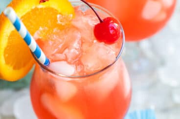 A hurricane cocktail with an orange slice garnish and a blue and white striped straw.