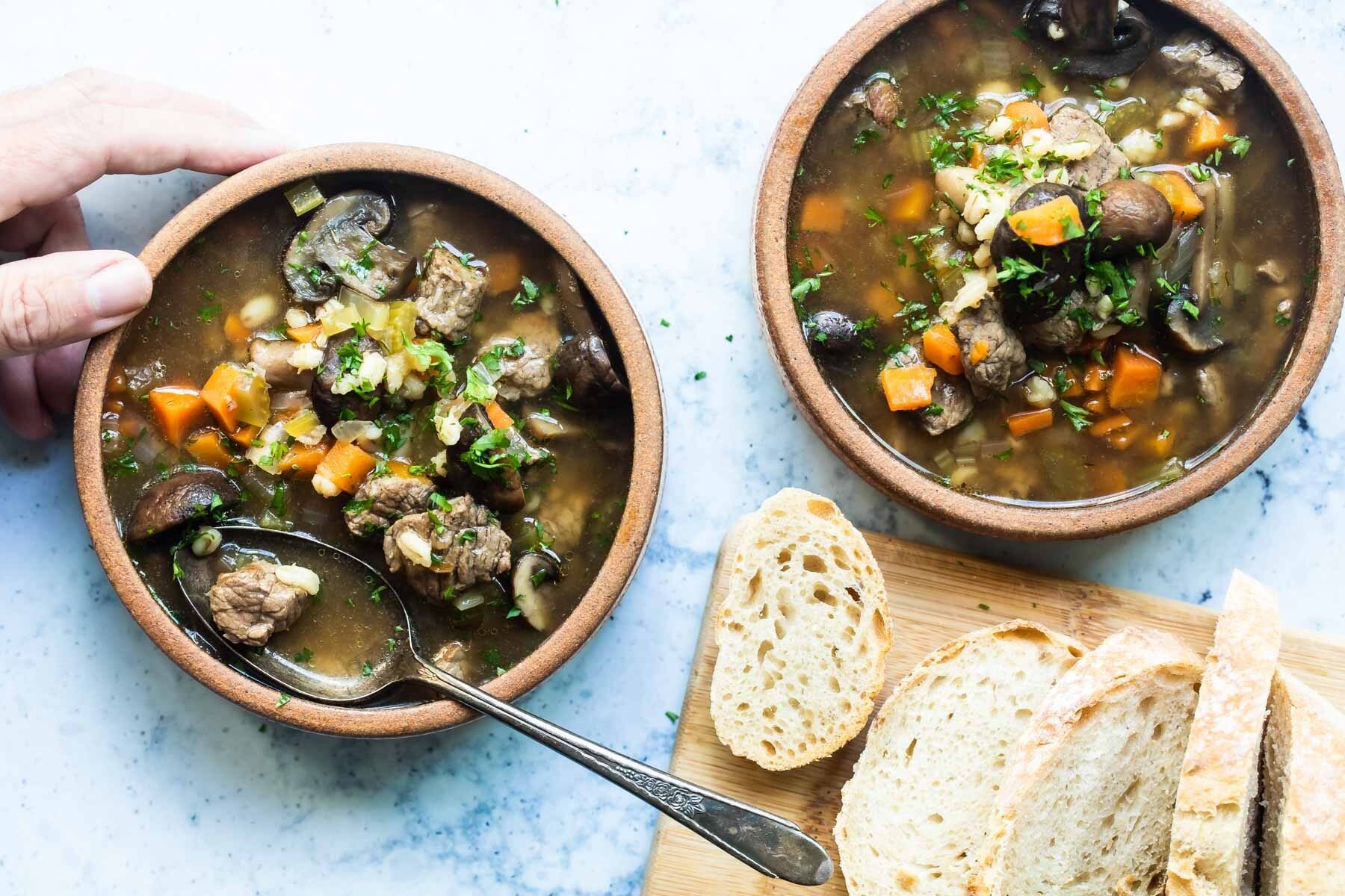 Slow cooker beef barley soup in two bowls.