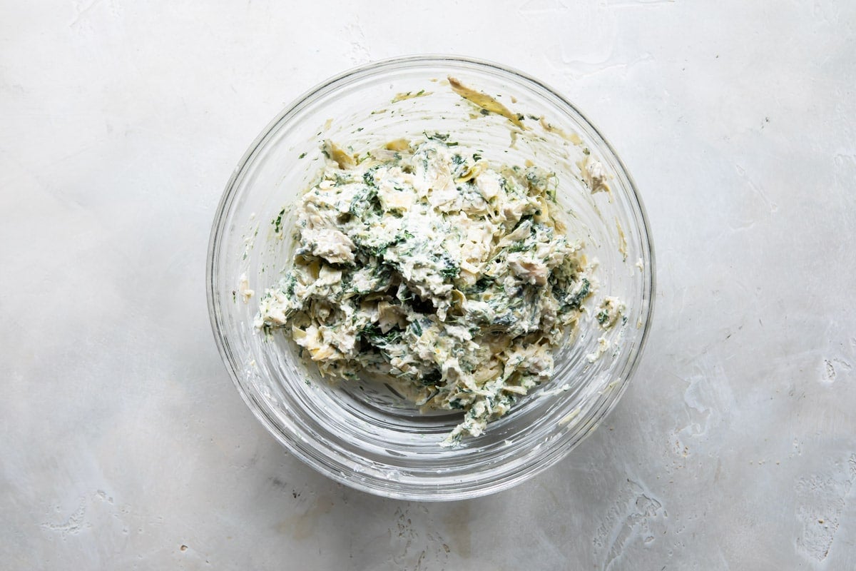 Spinach artichoke dip mixture in a clear bowl.