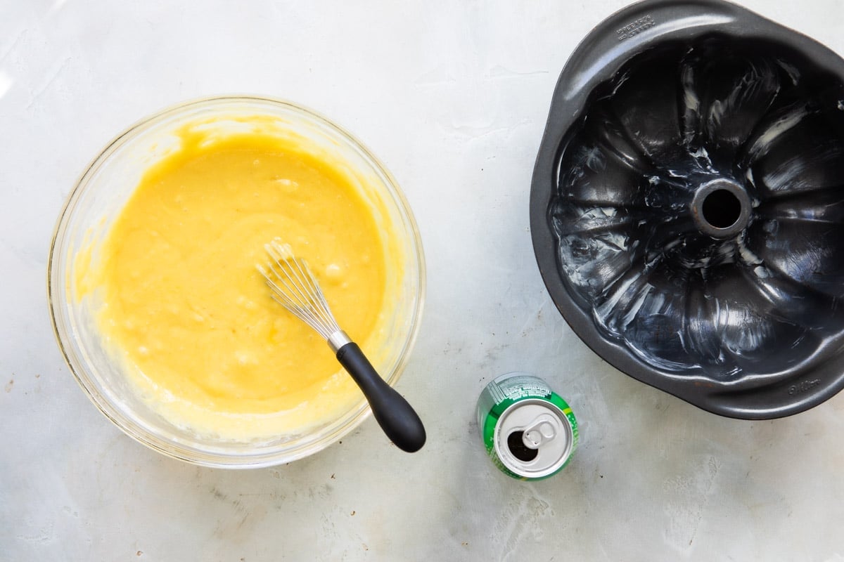 7 Up cake batter in a clear bowl next to a bundt cake pan.