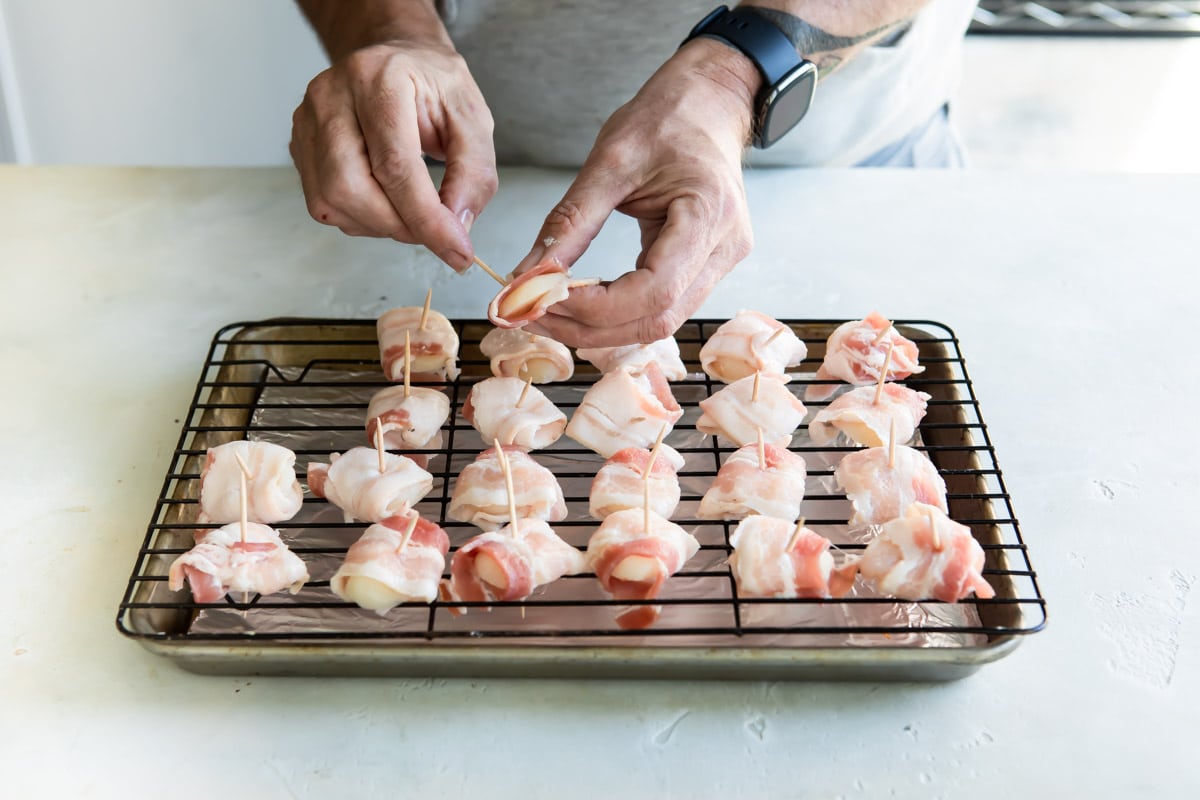 Someone wrapping bacon around water chestnuts and poking toothpicks through them to hold them together.