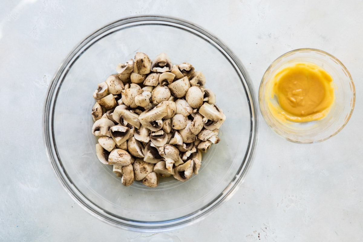 Mushrooms in a clear bowl next to a smaller clear bowl with a yellow mixture.