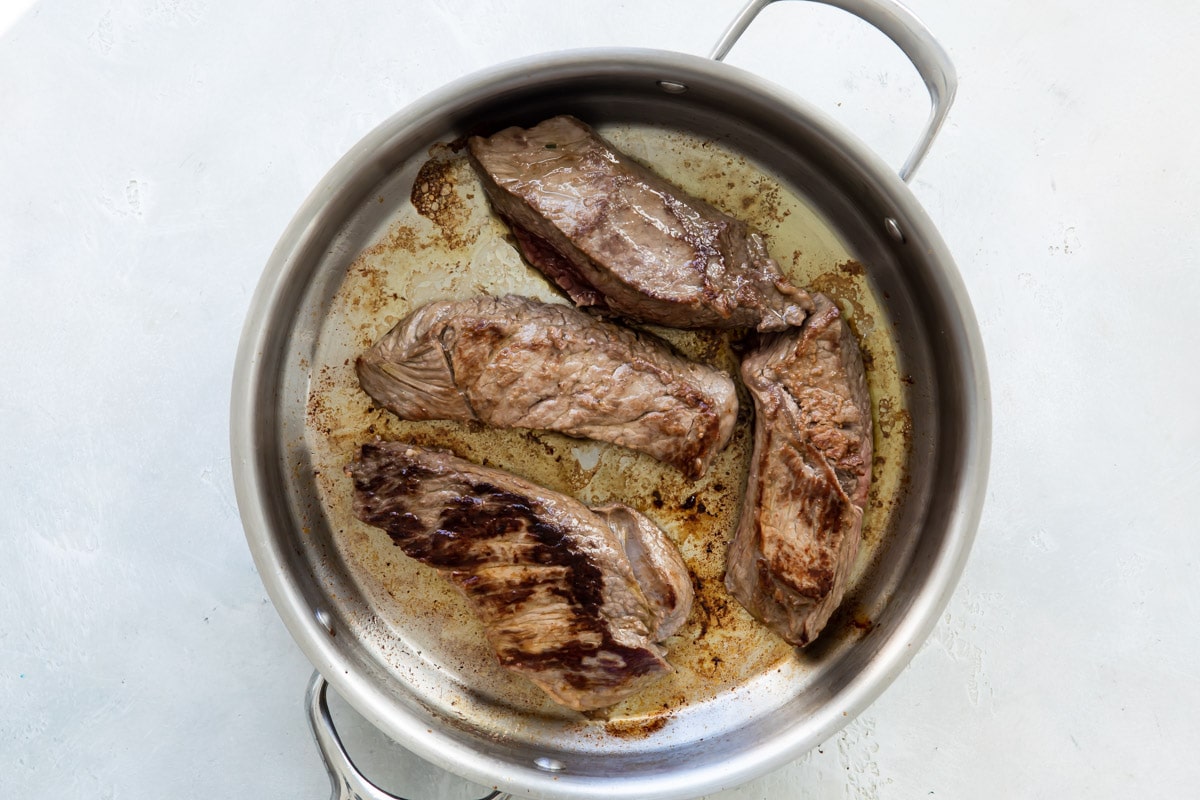 Four sirloin steak tip pieces in a skillet being cooked.
