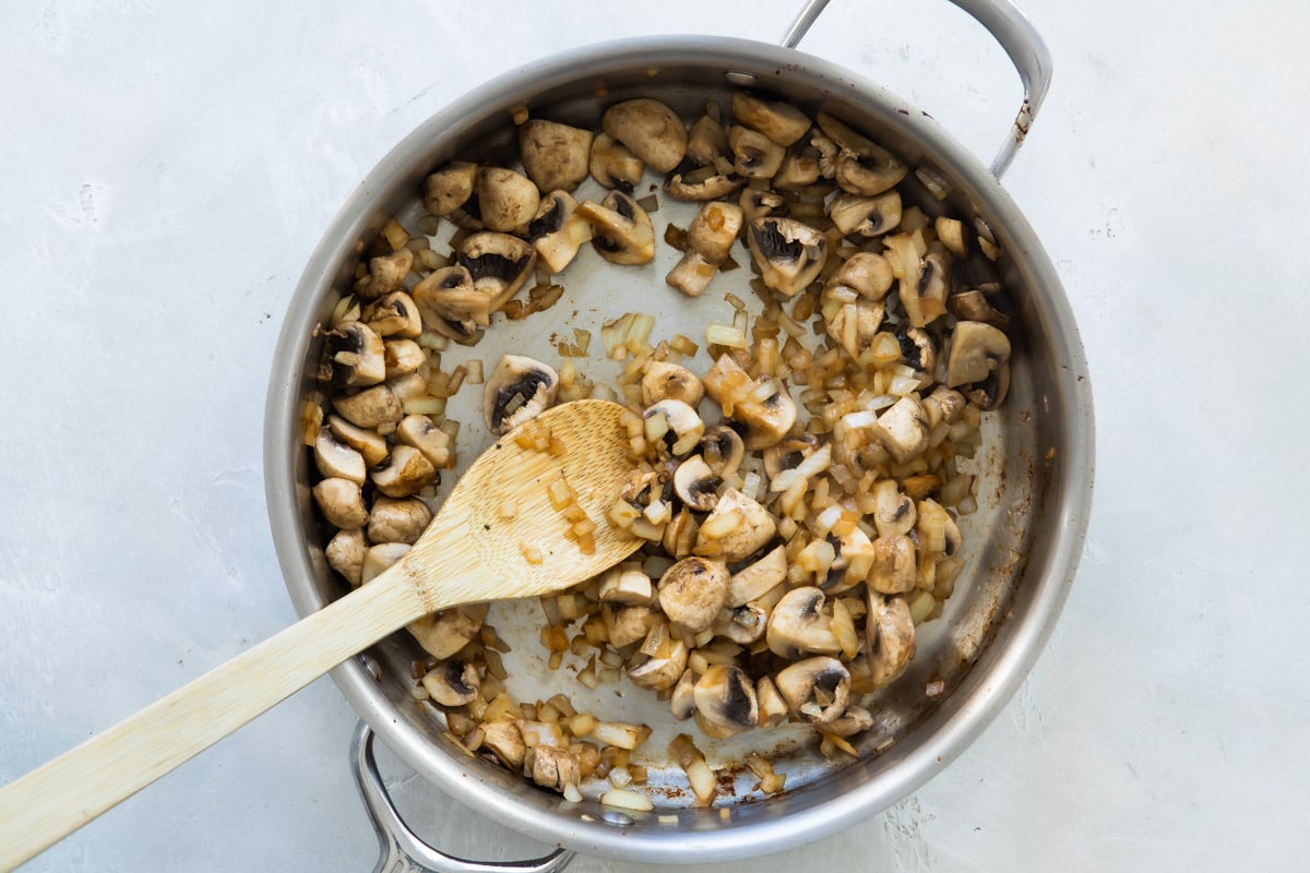 Mushrooms and onions being sauteed in a silver skillet.