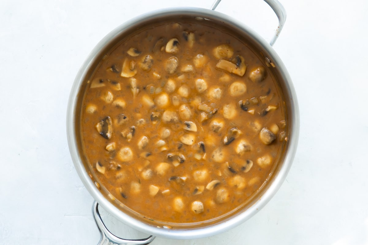 Mushrooms and stroganoff gravy in a silver skillet.
