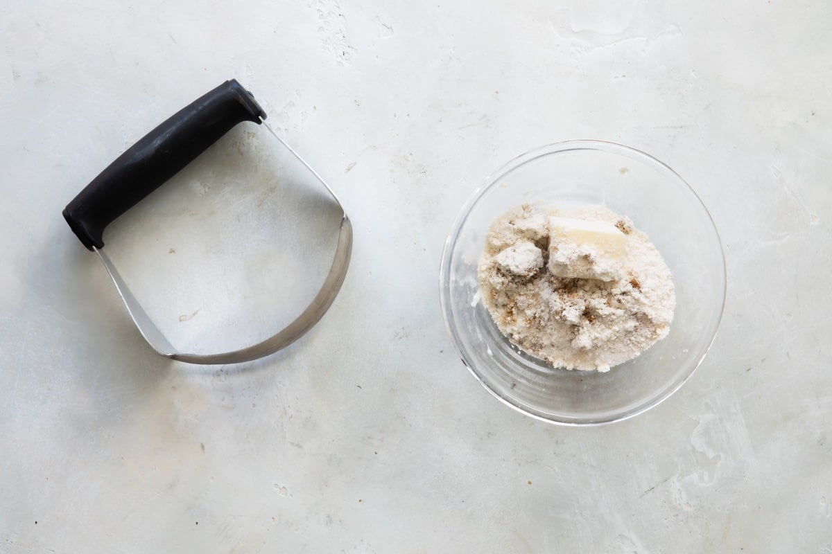 Streusel topping ingredients in a small glass bowl next to a pastry cutter.