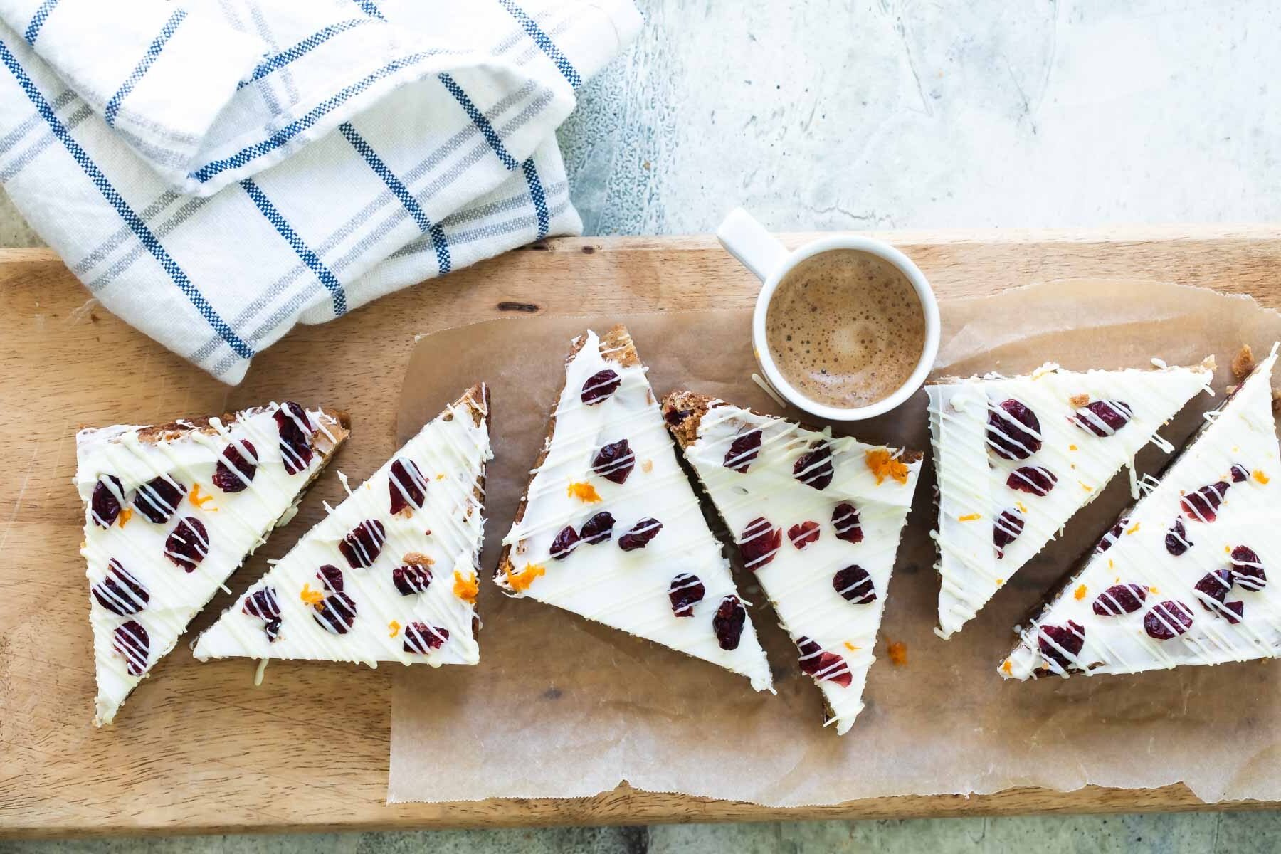 Six cranberry bliss bar triangles on a wooden cutting board.