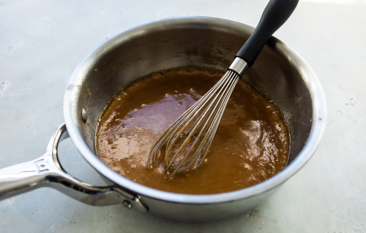 A skillet with a brown liquid and a whisk.