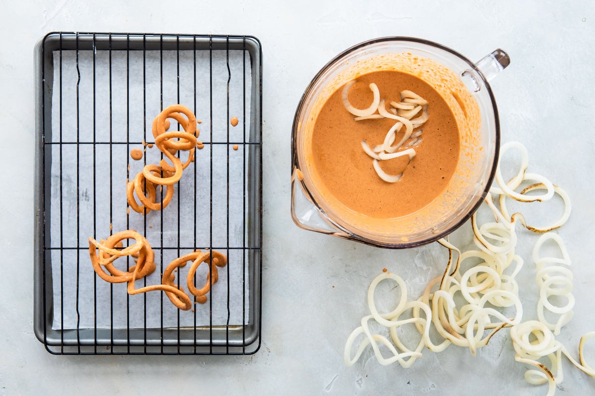 Potatoes being dipped in curly fry batter.