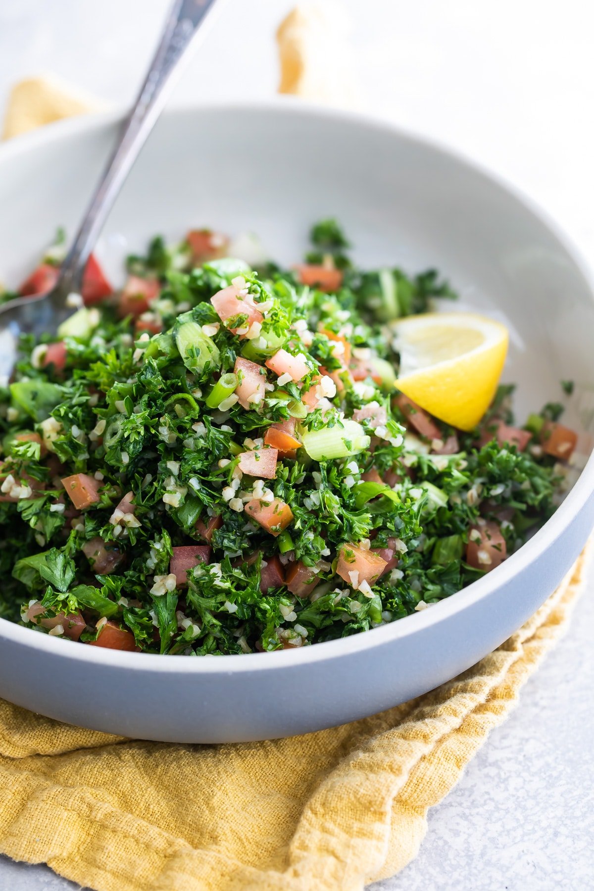 Bulgar tabbouleh in a white bowl with a lemon garnish.