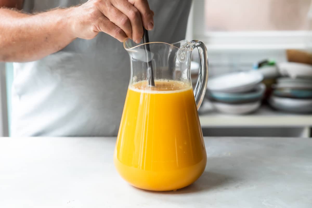 Someone stirring orange liquid in a glass carafe.