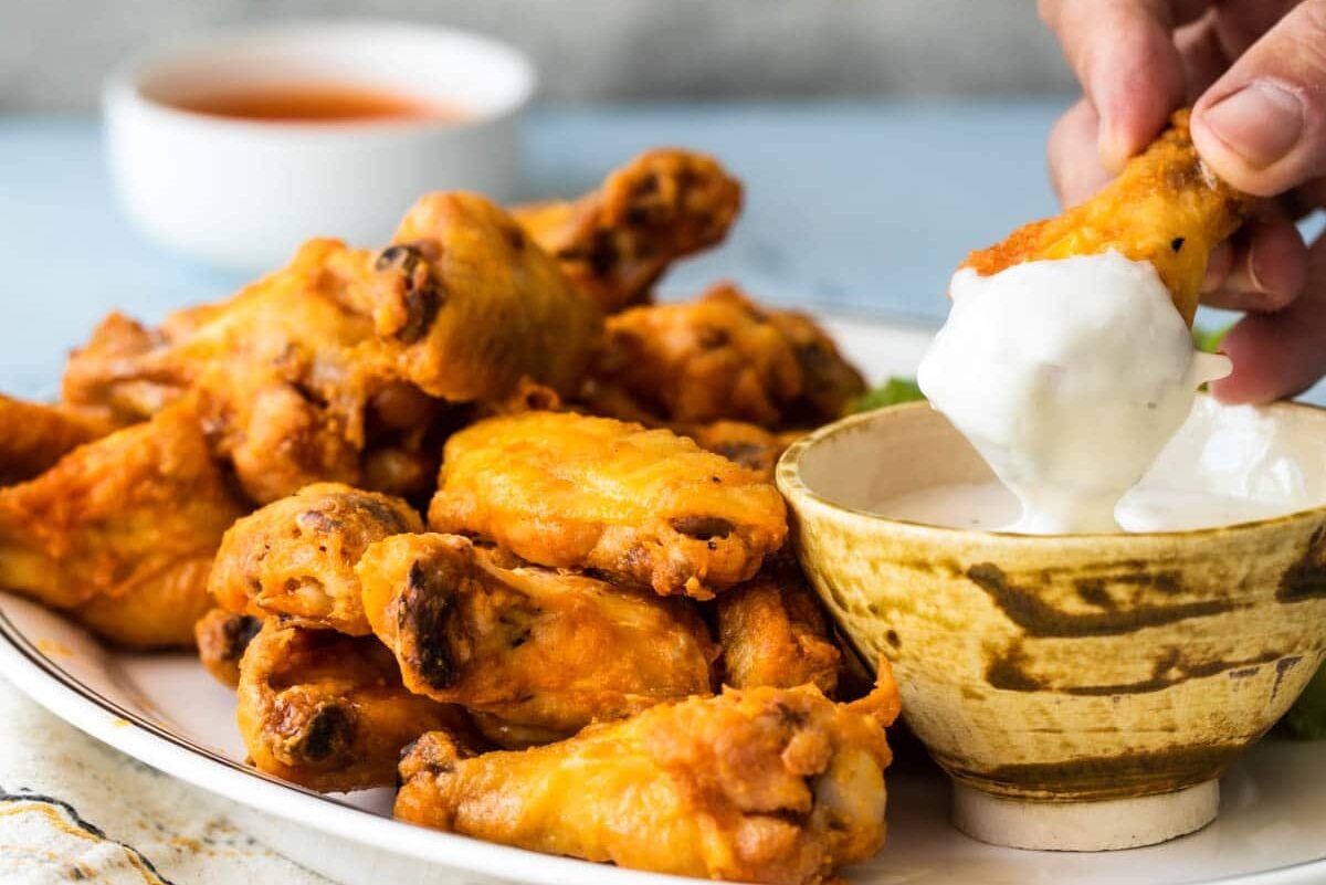 A chicken wing being dunked in blue cheese dressing.