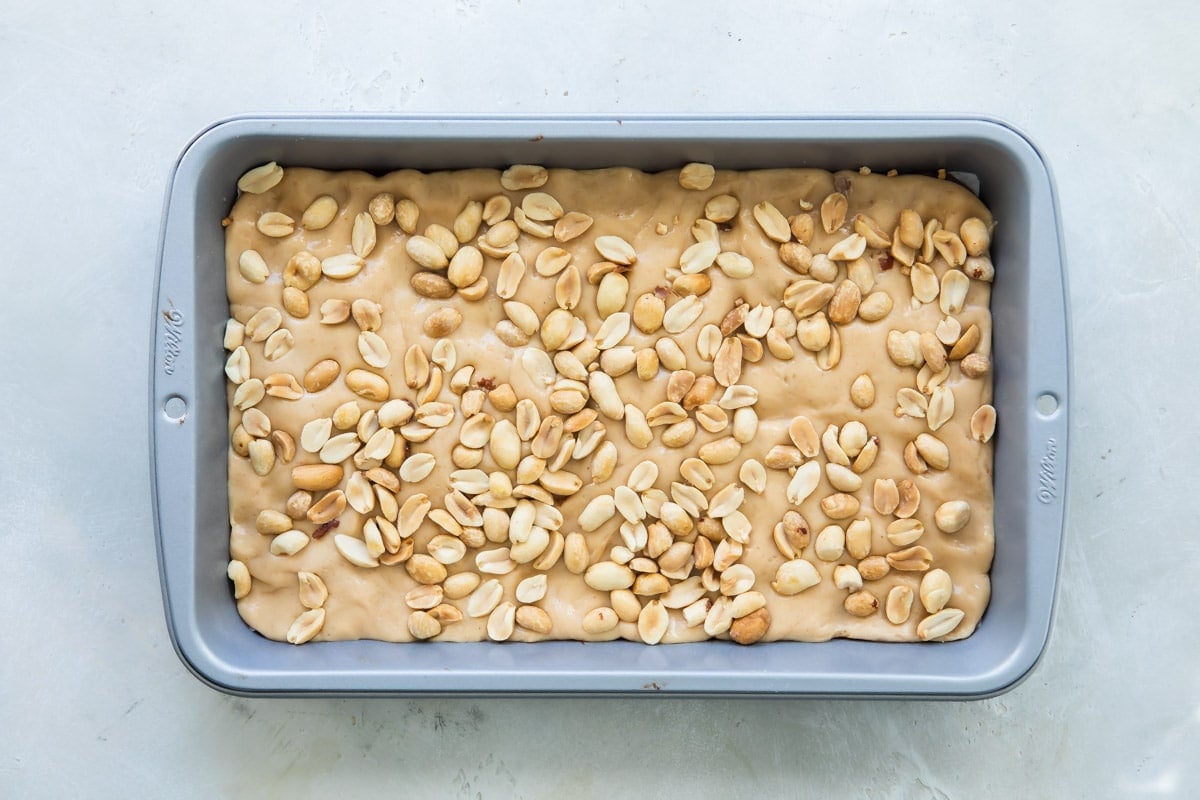 Peanuts spread over nougat in a baking pan.