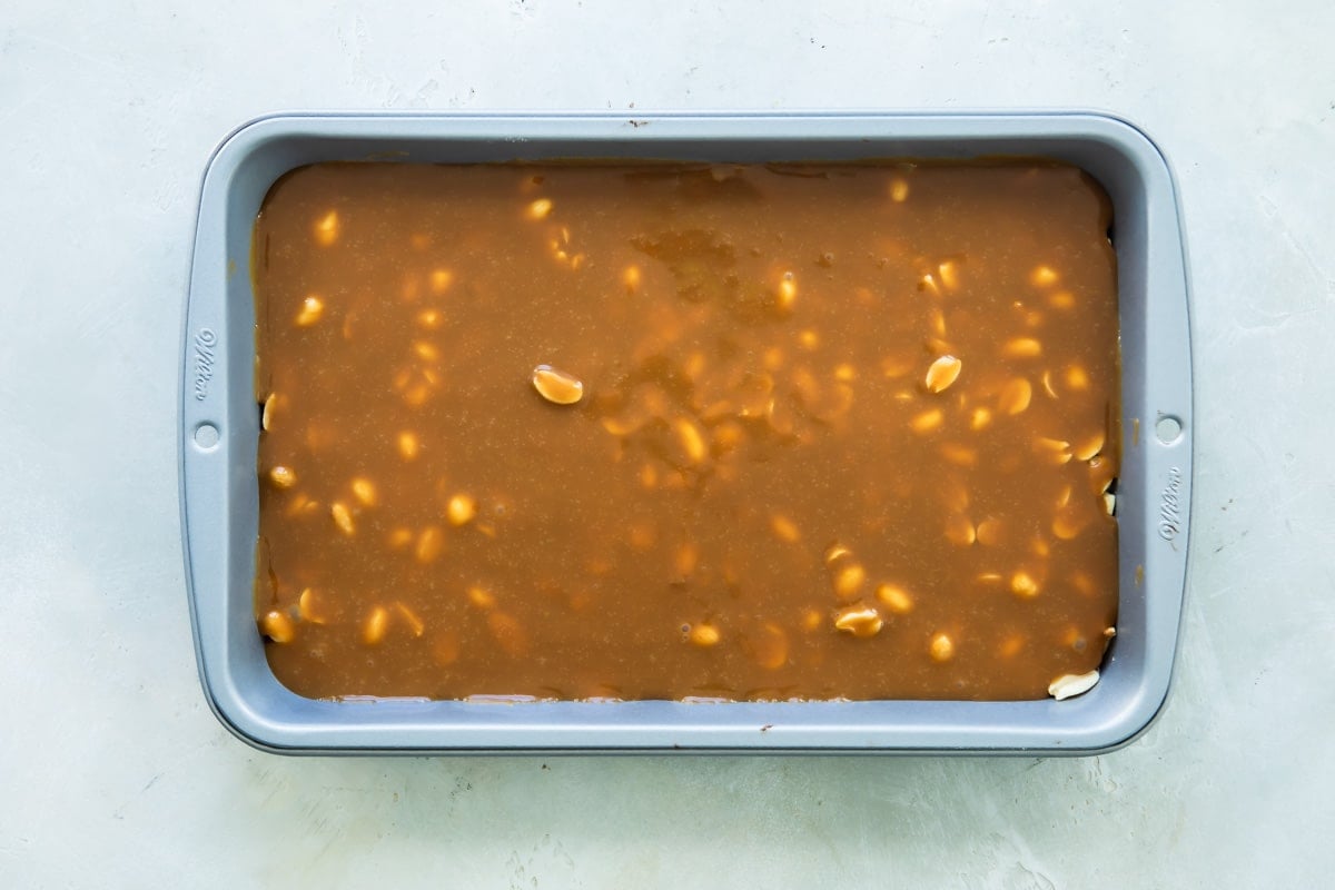 Caramel spread out over nougat and peanut layer in a baking pan.