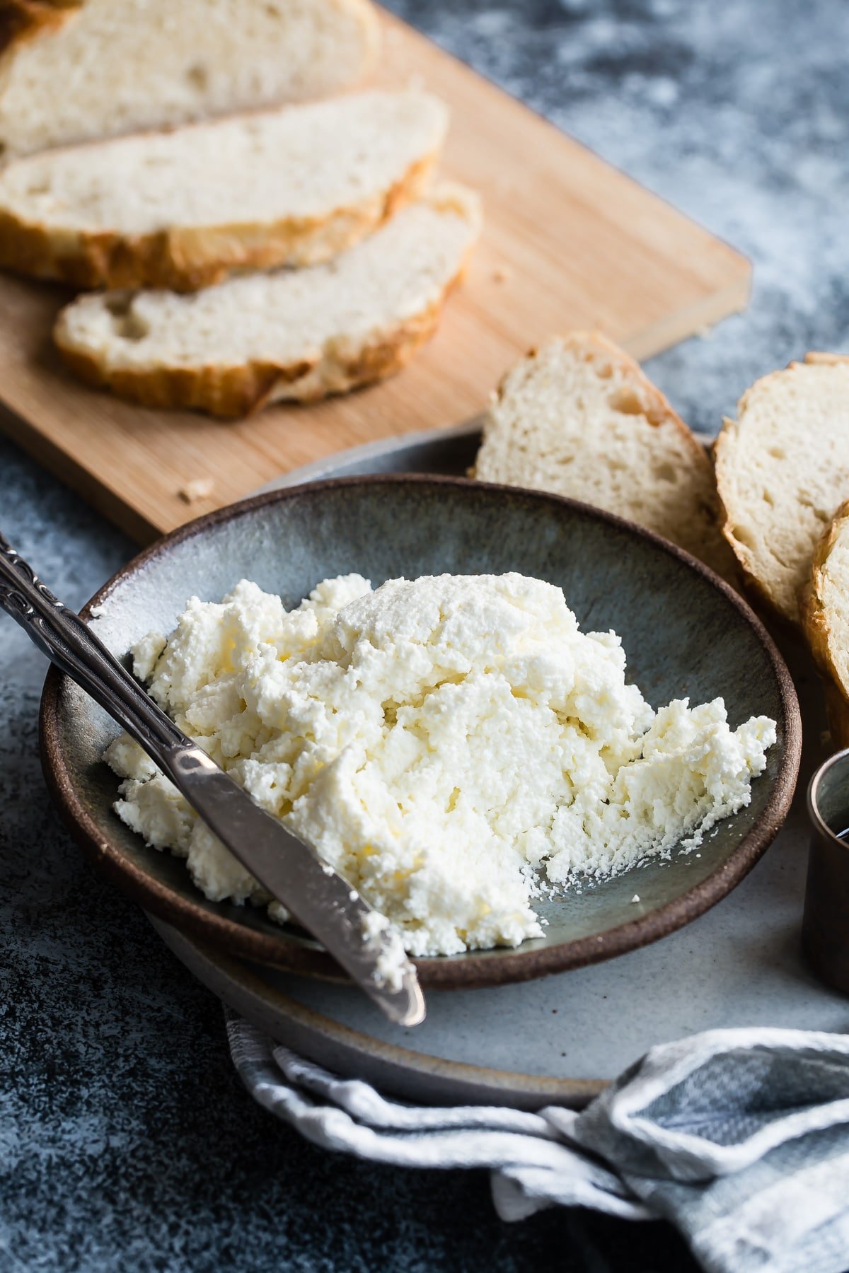 Homemade ricotta cheese in a blue bowl with a knife resting along the side.