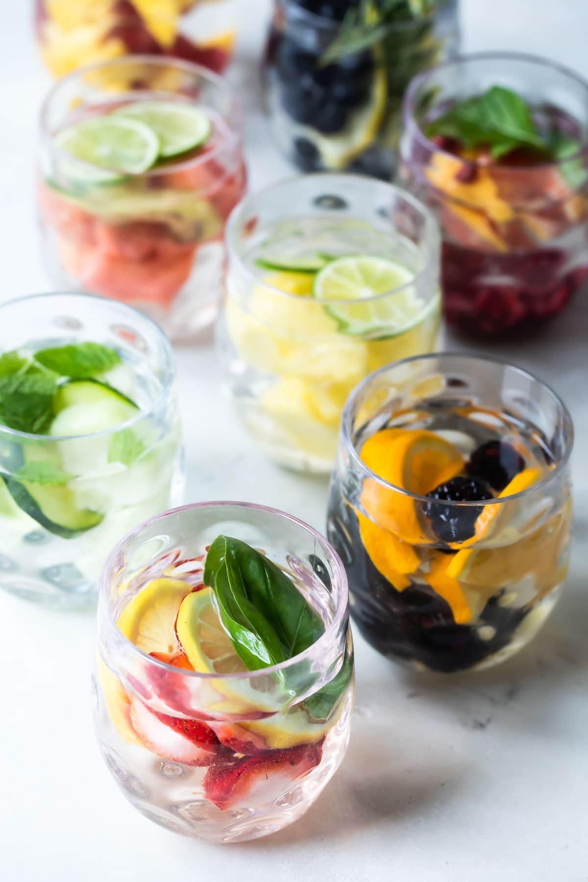 Glasses of water infused with fruit, vegetables, and fresh herbs.
