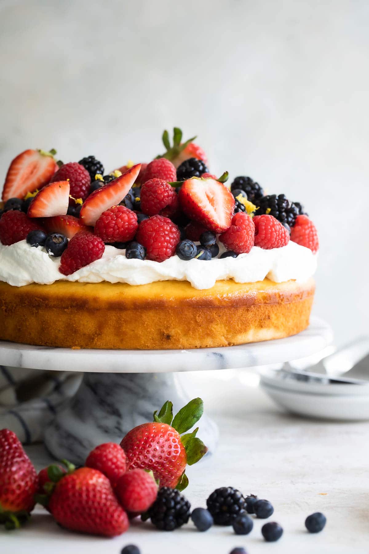 Lemon cake with limoncello cream and berries on top on a marble cake stand.