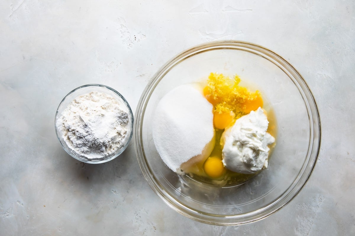 Dry ingredients in a bowl next to wet ingredients in a bowl for lemon cake with limoncello cream.