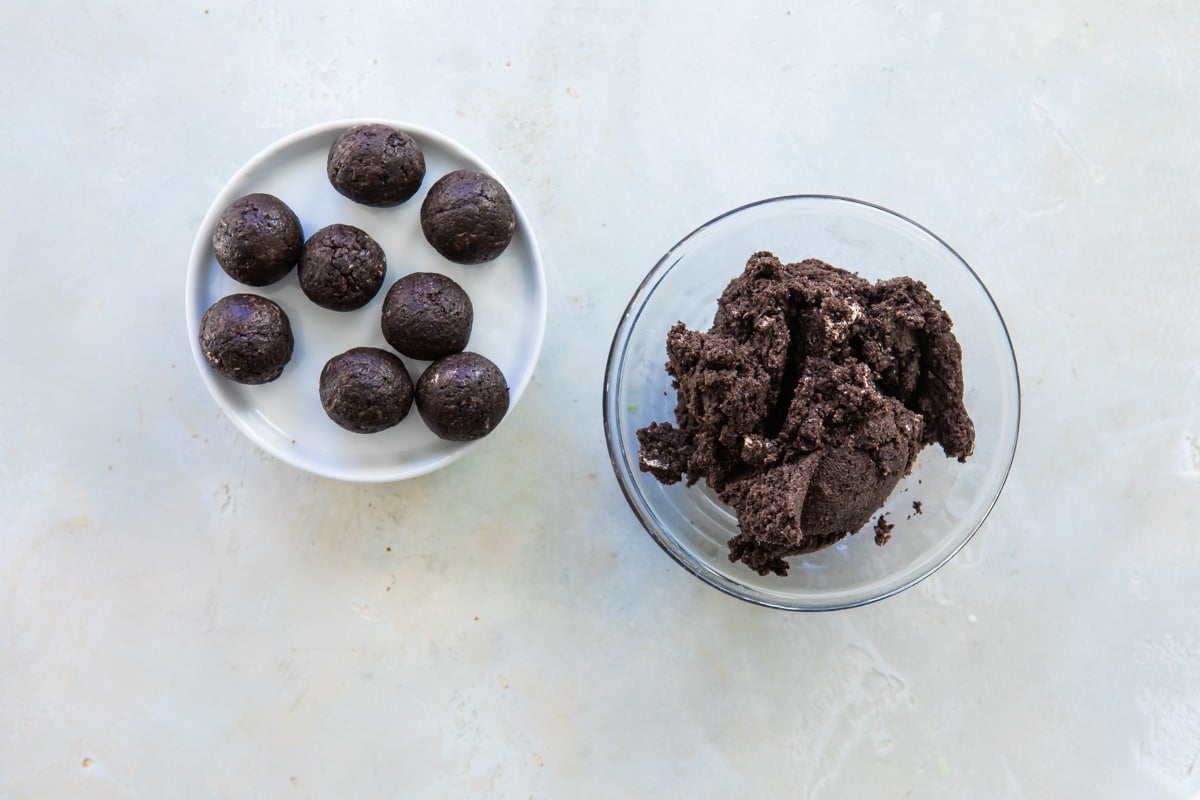 Oreo cookie ball dough in a bowl next to a plate of rolled oreo cookie balls.
