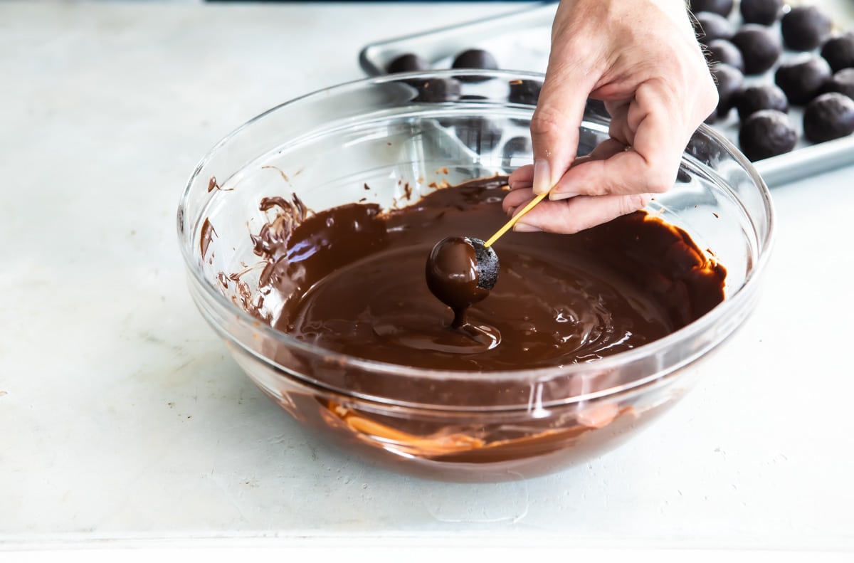 Someone dipping an Oreo cookie ball in melted chocolate.